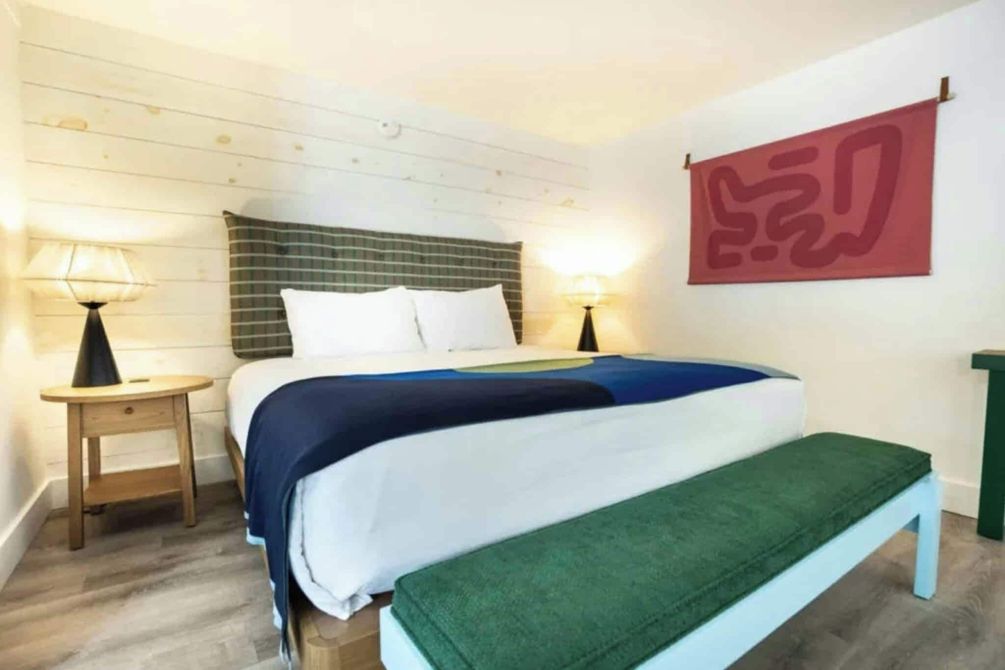 Un dormitorio con cama, mesitas de noche, un banco y una obra de arte colgada en la pared.