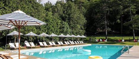 Una piscina con sillas de descanso y sombrillas, rodeada de árboles.