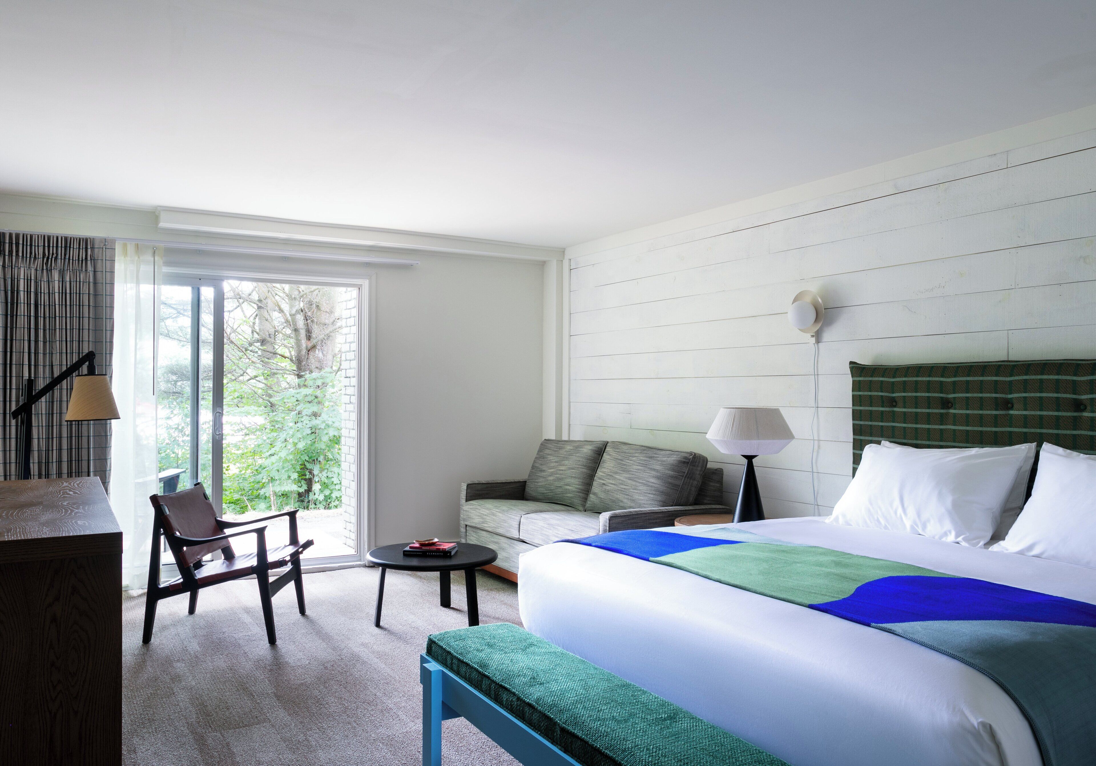 A hotel room with a bed, a sofa, a chair, a small table, and a lamp.