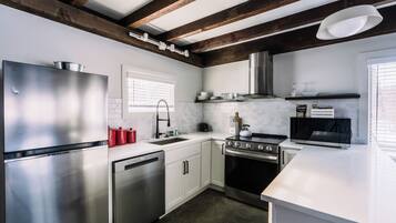 A modern kitchen with stainless steel appliances, white cabinetry, and a wooden ceiling beam structure.