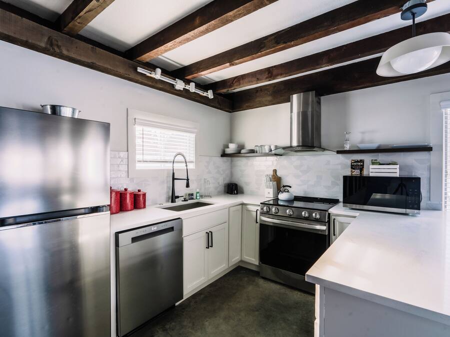 A modern kitchen with stainless steel appliances, white cabinetry, and a wooden ceiling beam structure.