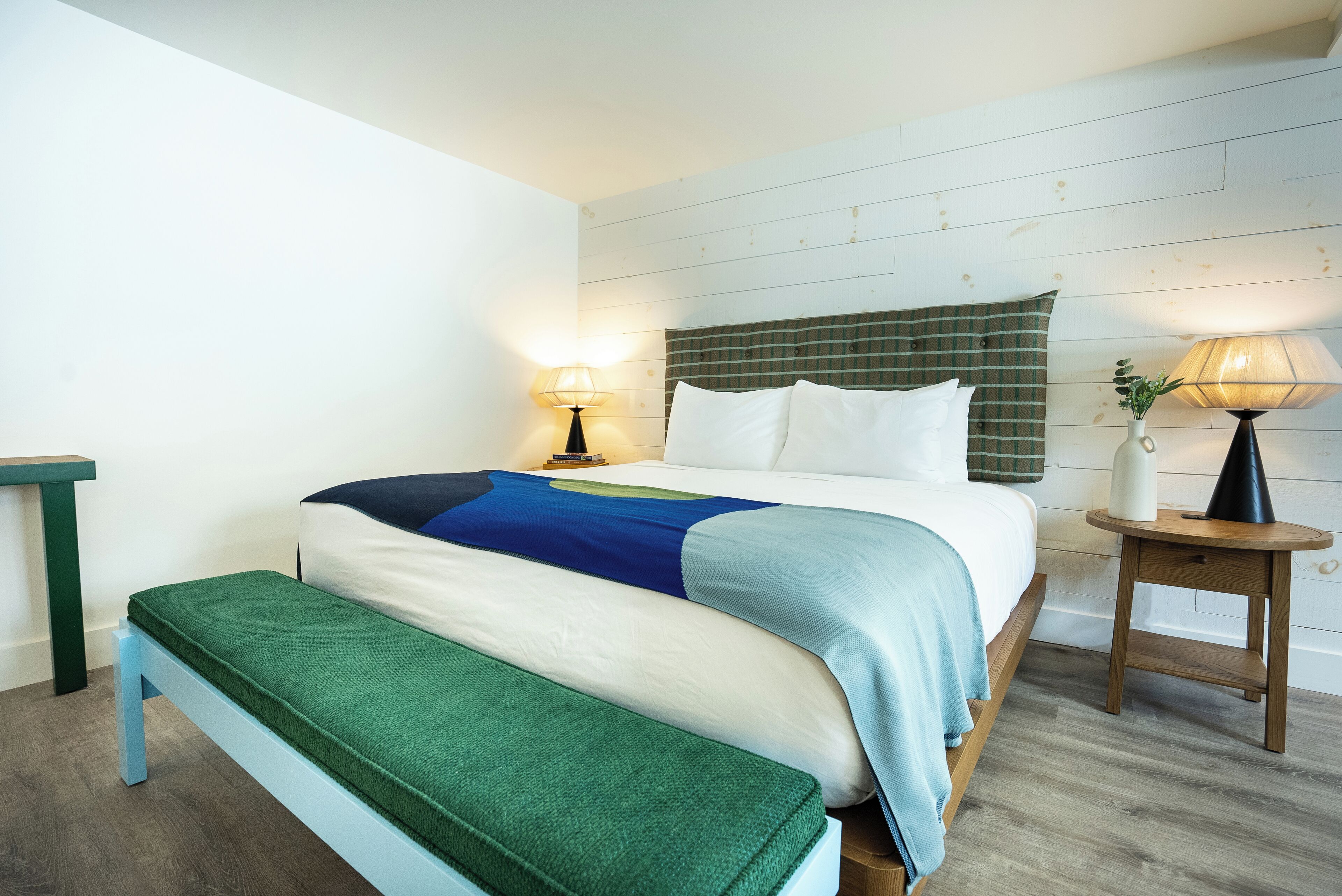 Un dormitorio ordenado con cama, mesitas de noche y un banco.