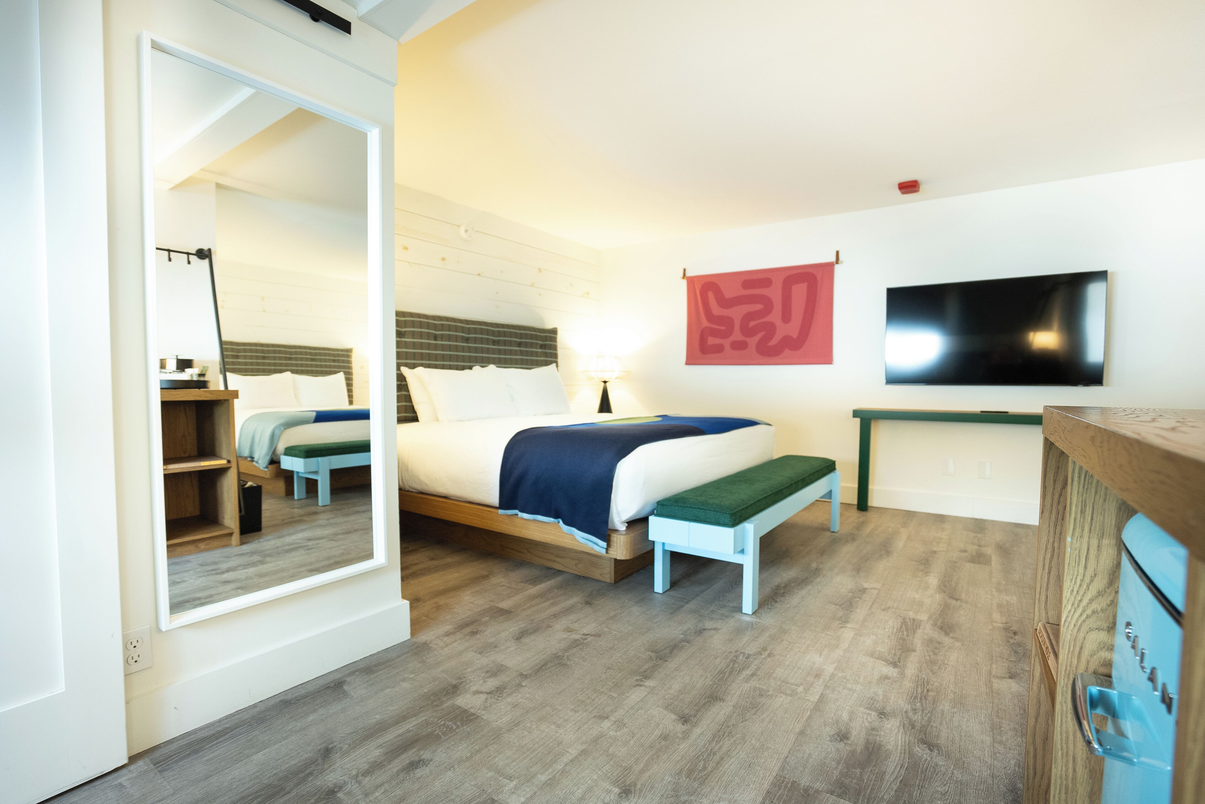 Un dormitorio con cama, un banco, un televisor y un espejo.