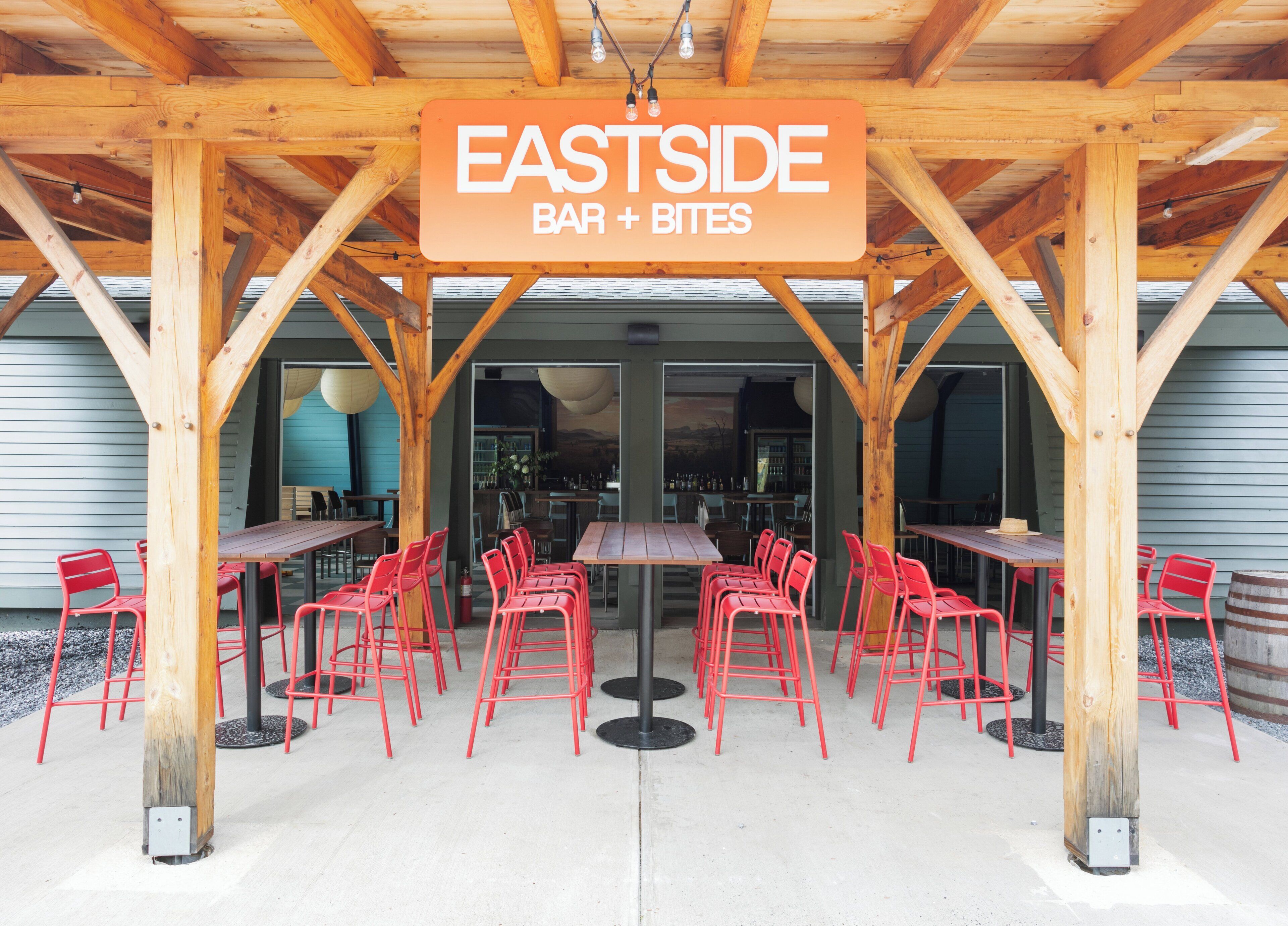 A wooden outdoor seating area with tables and red chairs, labeled "EASTSIDE BAR + BITES".