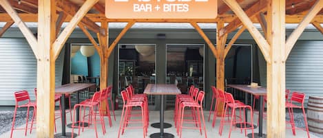 A wooden outdoor seating area with tables and red chairs, labeled "EASTSIDE BAR + BITES".