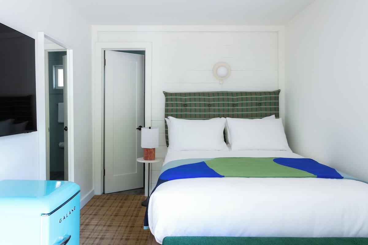 Una habitación de hotel con una cama, una mesita de noche, una lámpara y una maleta azul.
