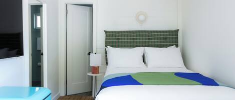 Ett hotellrum med en säng, ett sängbord, en lampa och en blå resväska.