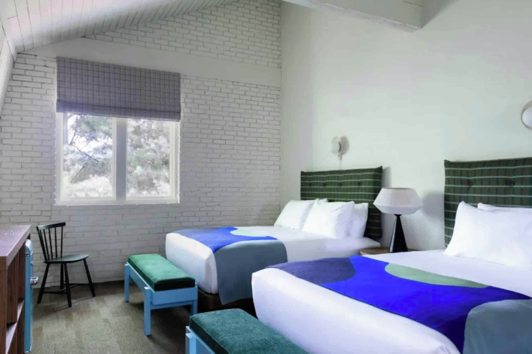 A hotel room with two beds, a desk, a chair, and a window.
