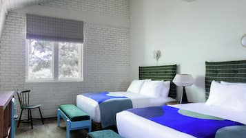 A hotel room with two beds, a desk, a chair, and a window with a view of trees.