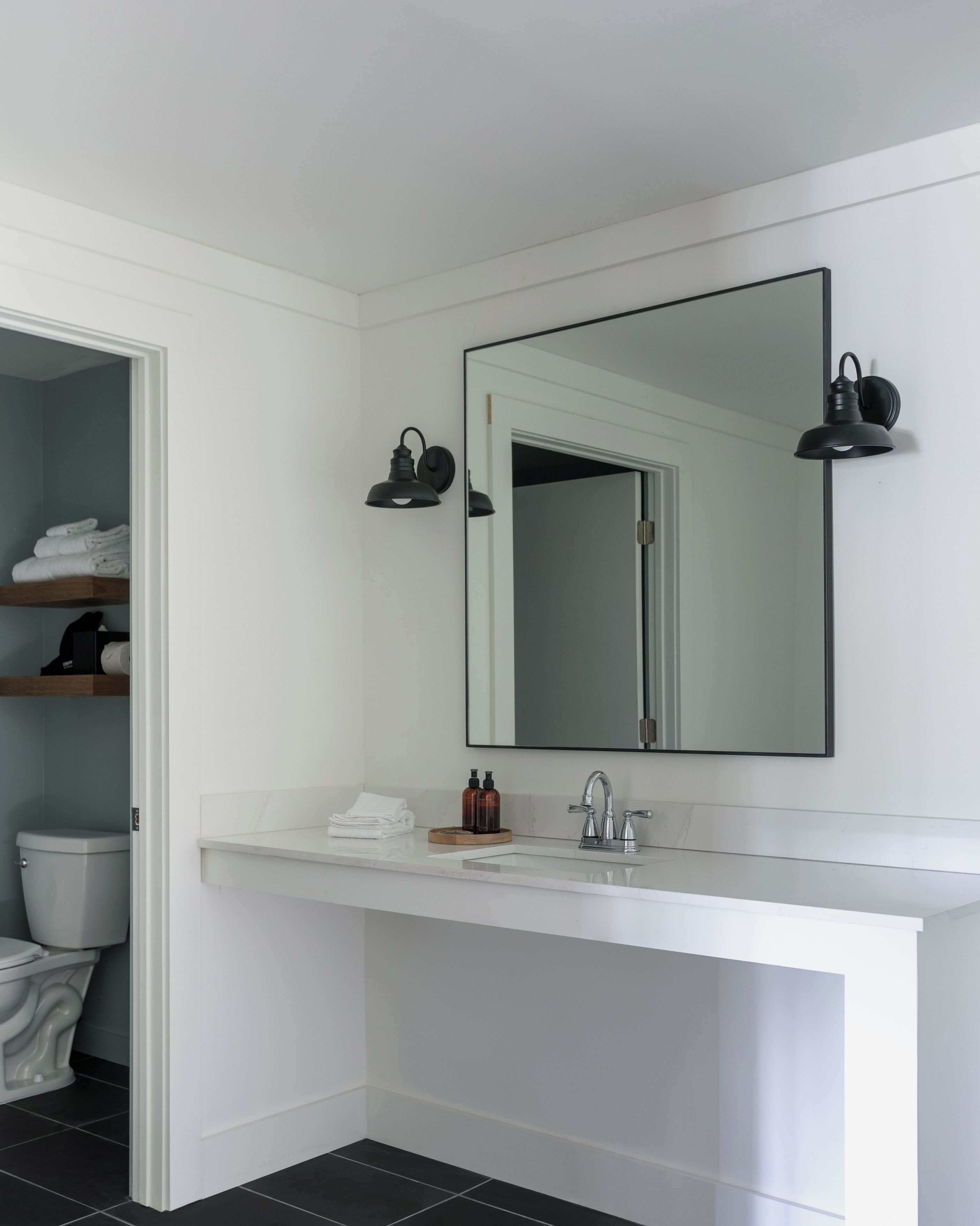 Een moderne badkamer met een wit wastafelmeubel, een grote spiegel en twee wandlampen.