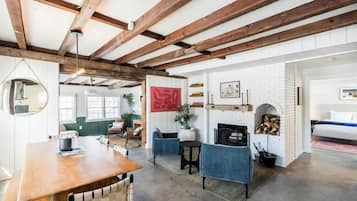 A spacious room with exposed wooden beams, a fireplace, a round mirror, and a dining area.