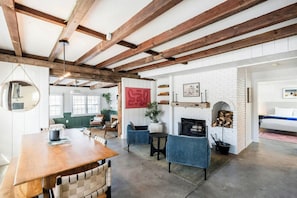 A spacious room with exposed wooden beams, a fireplace, a round mirror, and a dining area.