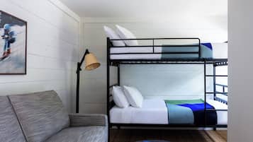 A bunk bed with white bedding, a grey sofa, and a floor lamp.