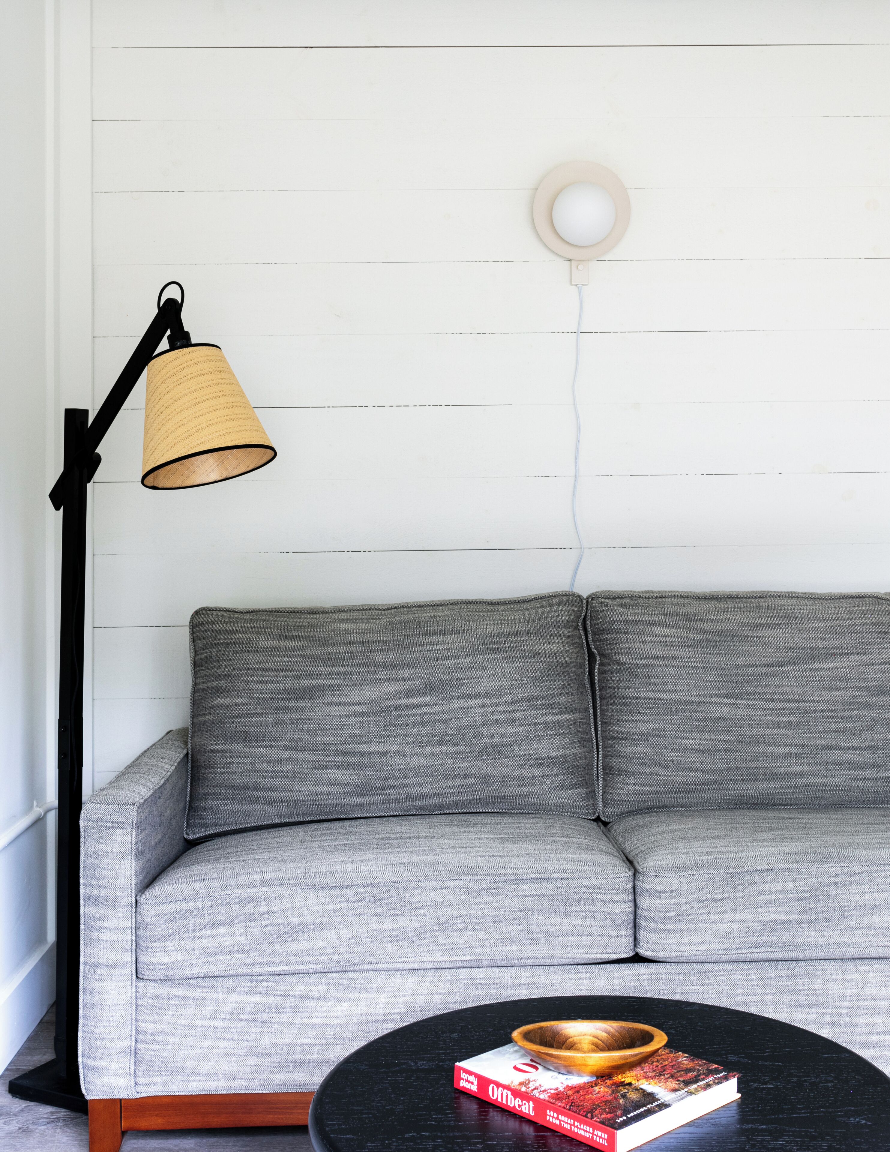 A grey sofa with a black floor lamp and a book on a black table.