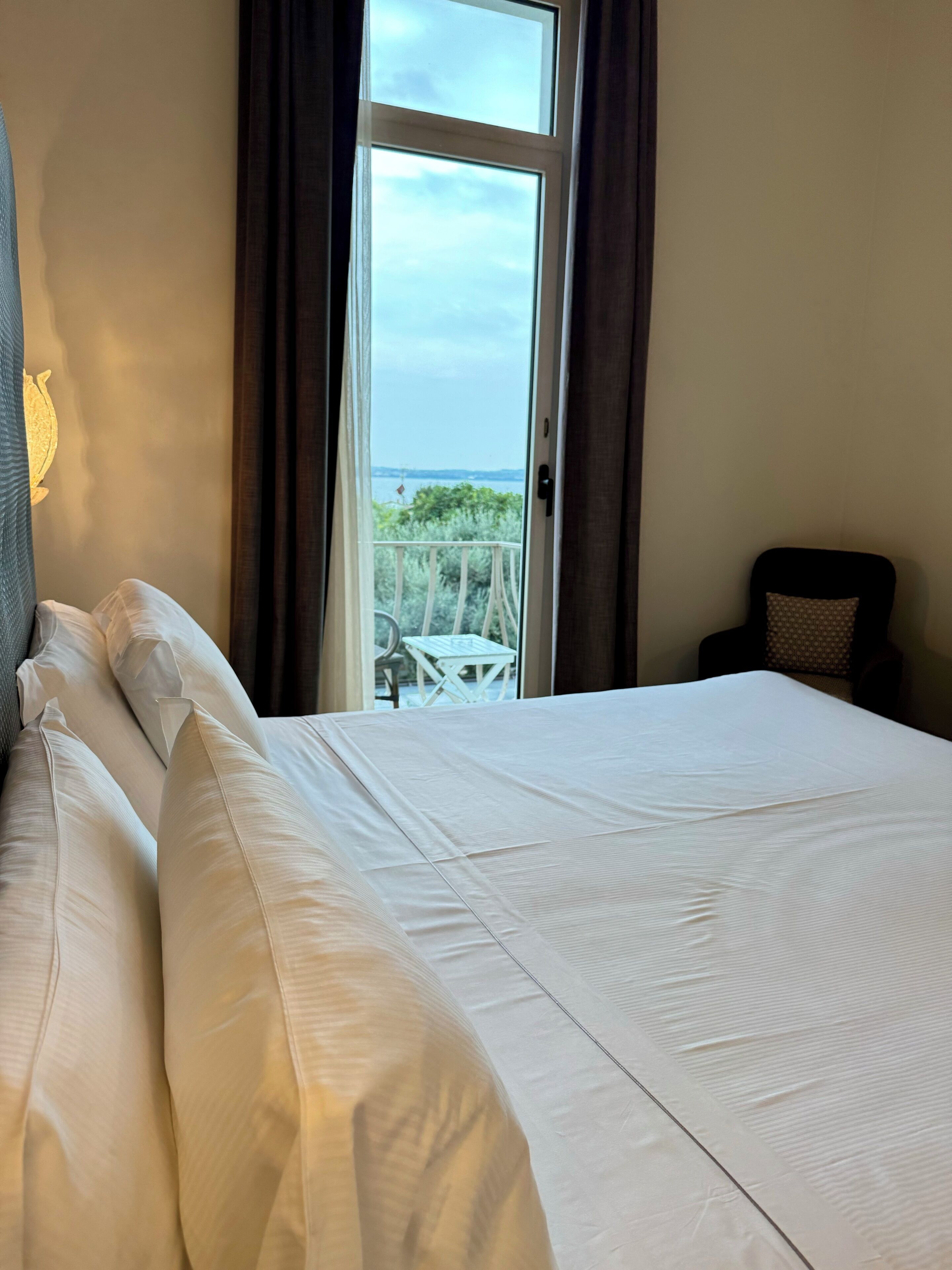 A hotel room with a large bed, a chair, and a view of the outdoors through a glass door.