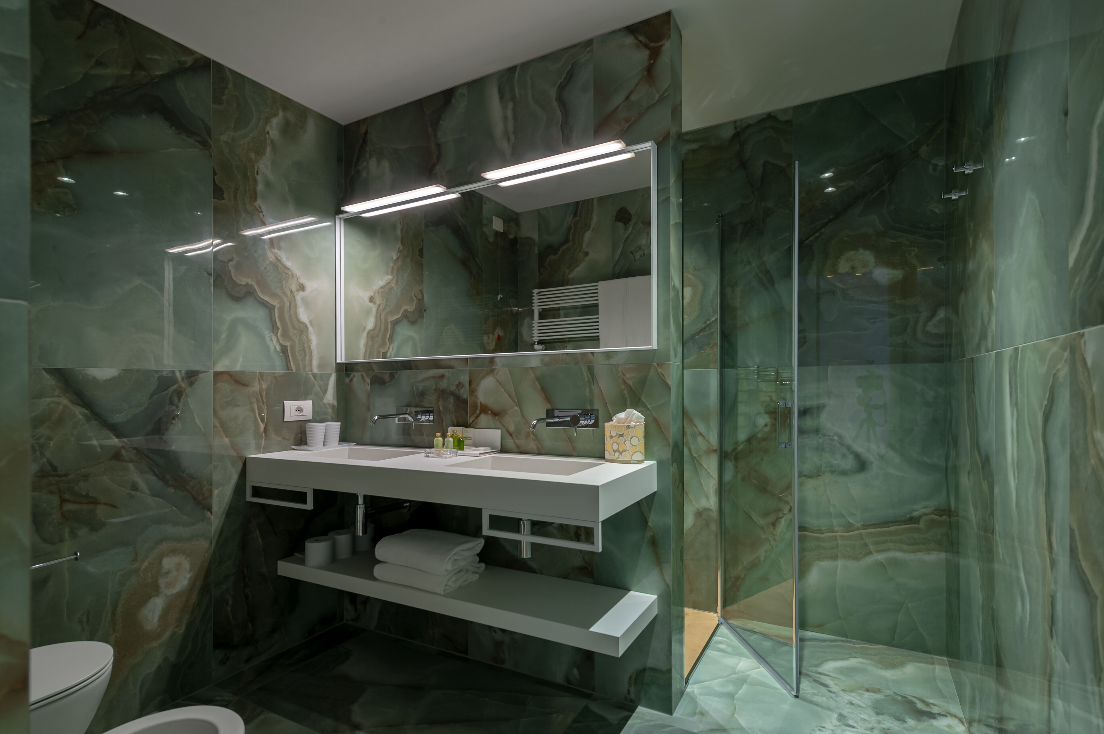 Un baño moderno con salpicadero de mármol, cabina de ducha con mampara de vidrio y tocador con espejo.