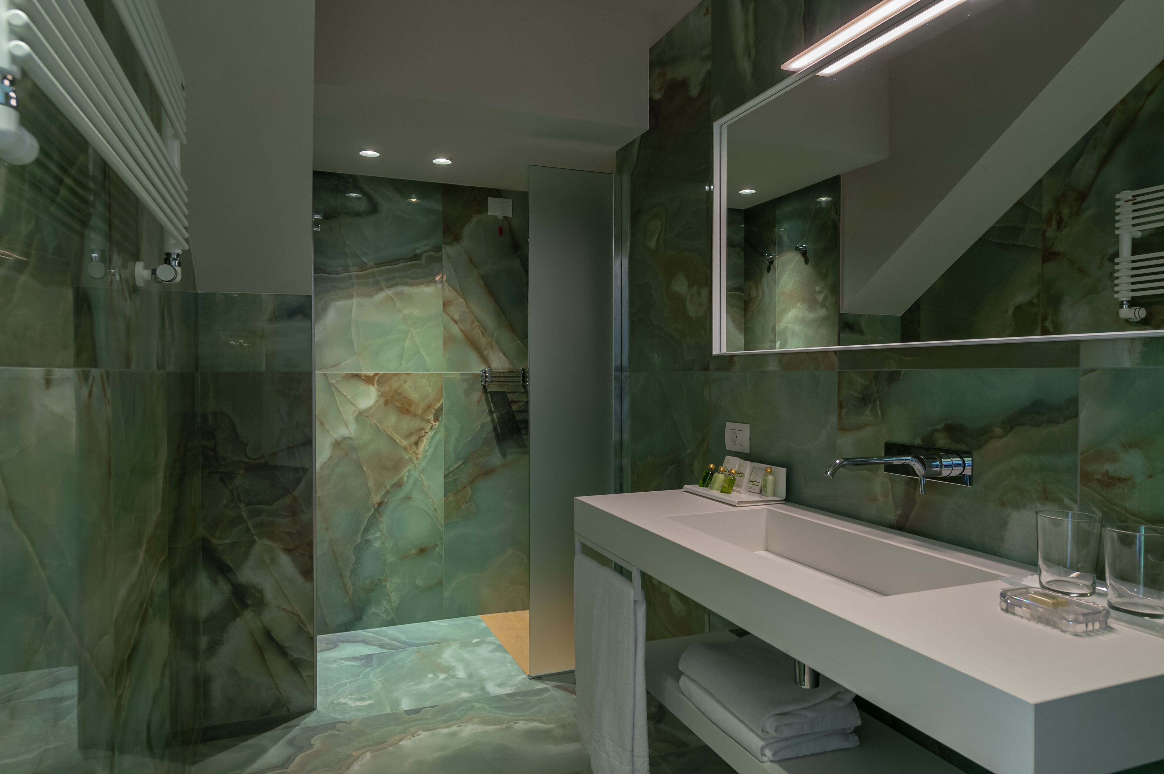 Un baño moderno con pared de mármol, un espejo grande, un tocador blanco y una cabina de ducha con mampara de vidrio.