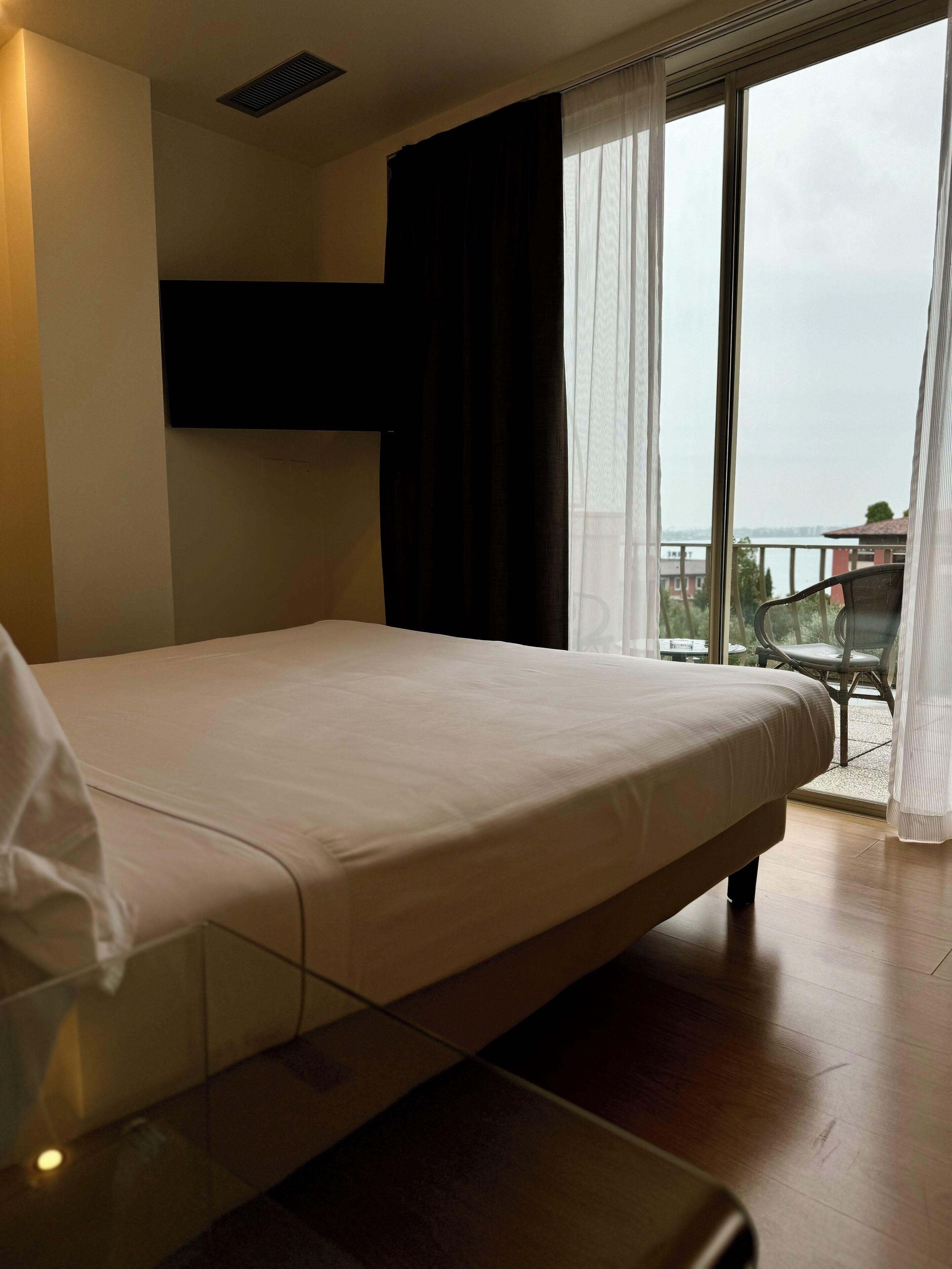 Een hotelkamer met een bed, een aan de muur bevestigde televisie en uitzicht op de omgeving door een groot raam.