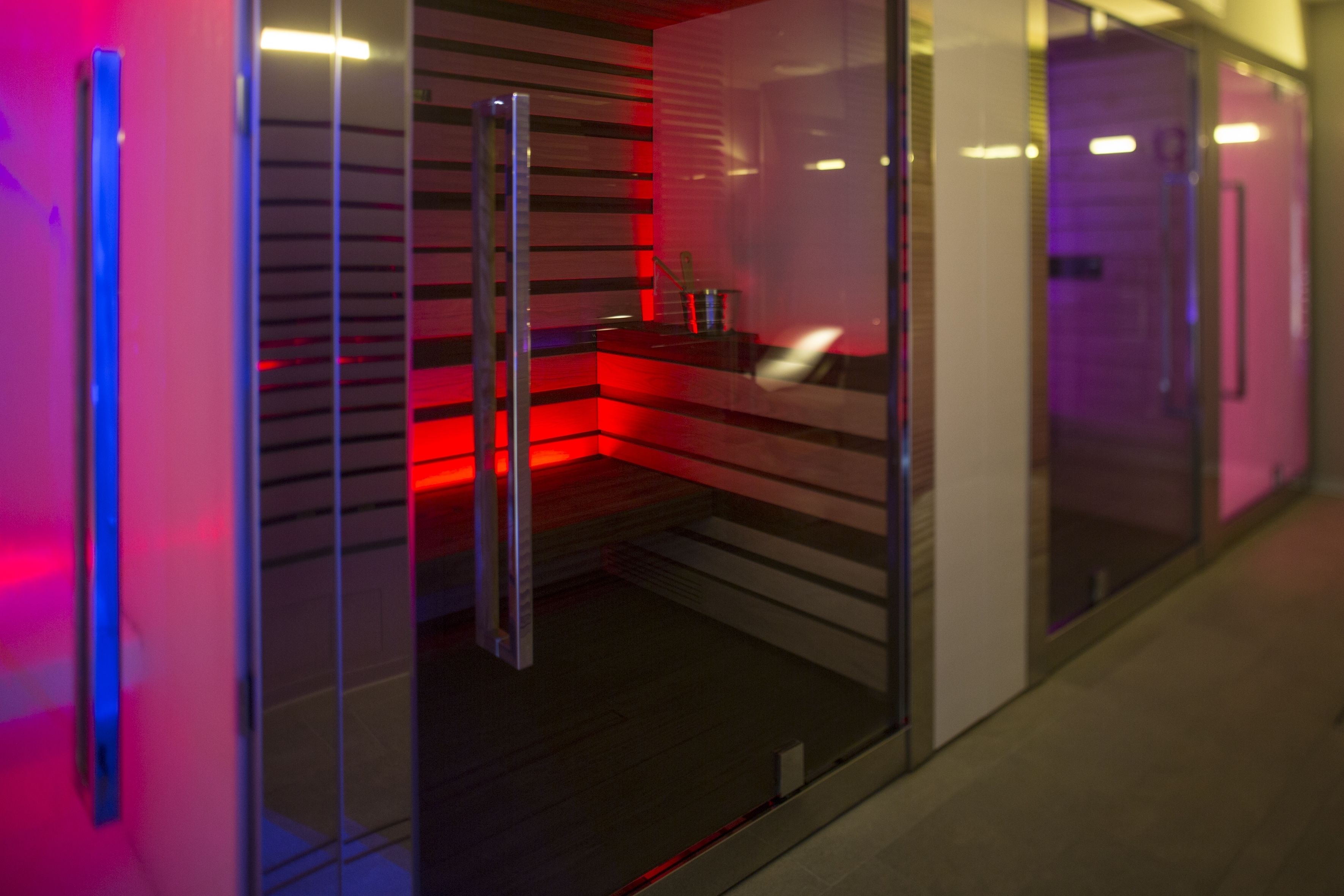 Una cocina moderna con puerta de cristal, iluminación roja y un refrigerador de acero inoxidable.
