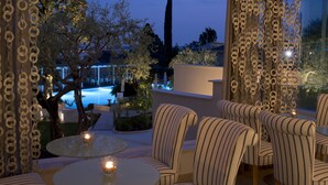 A terrace with striped chairs and a table, overlooking a pool and trees. -  Olivi Hotel & Natural Spa (Sirmione)