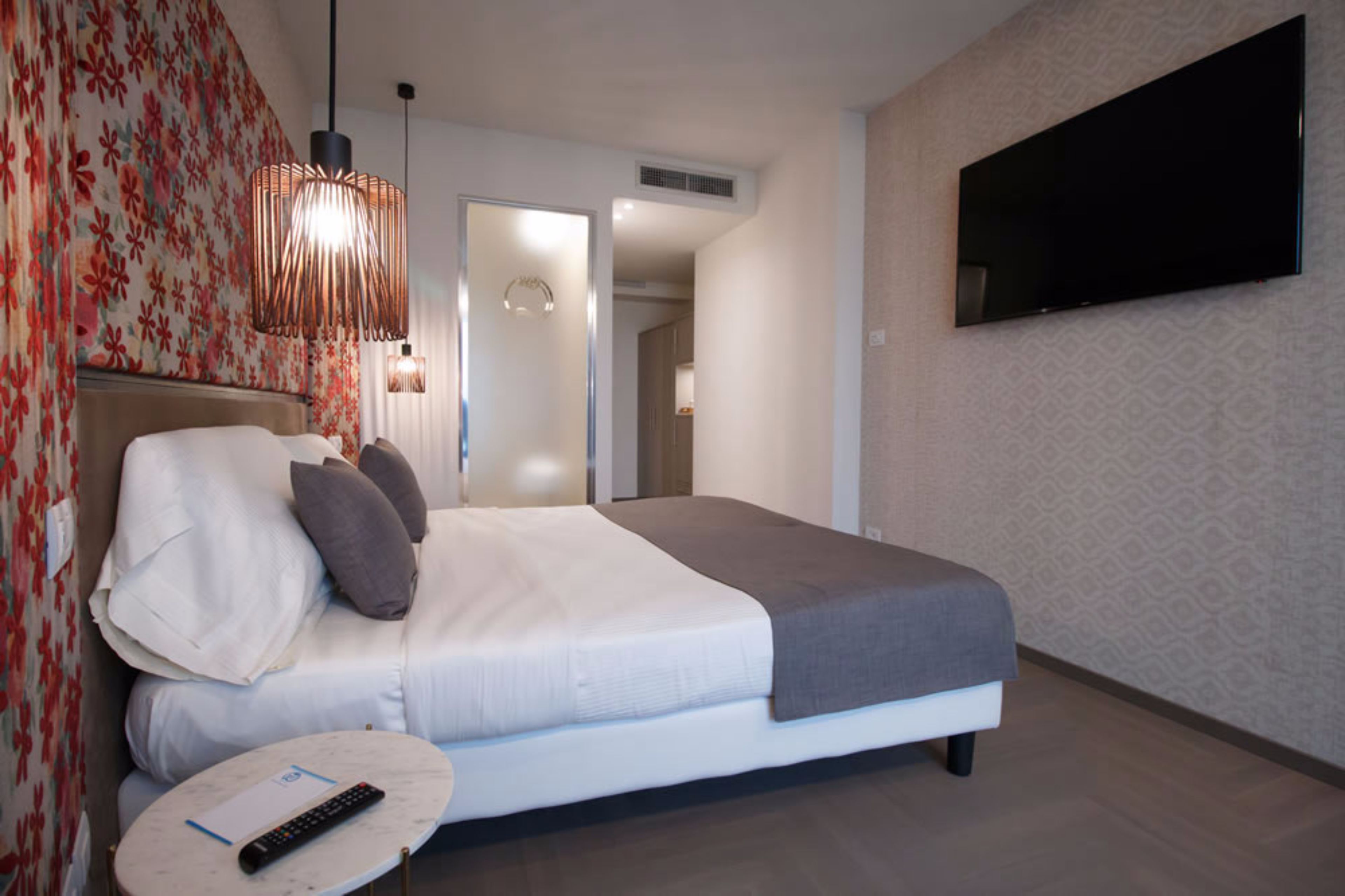 Ein modernes Hotelzimmer mit einem Bett, einem an der Wand montierten Fernseher und einer Fernbedienung auf einem Nachttisch.