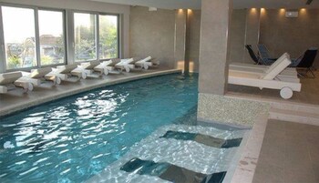An indoor swimming pool with clear water, lounge chairs along the poolside, and a view of greenery outside.