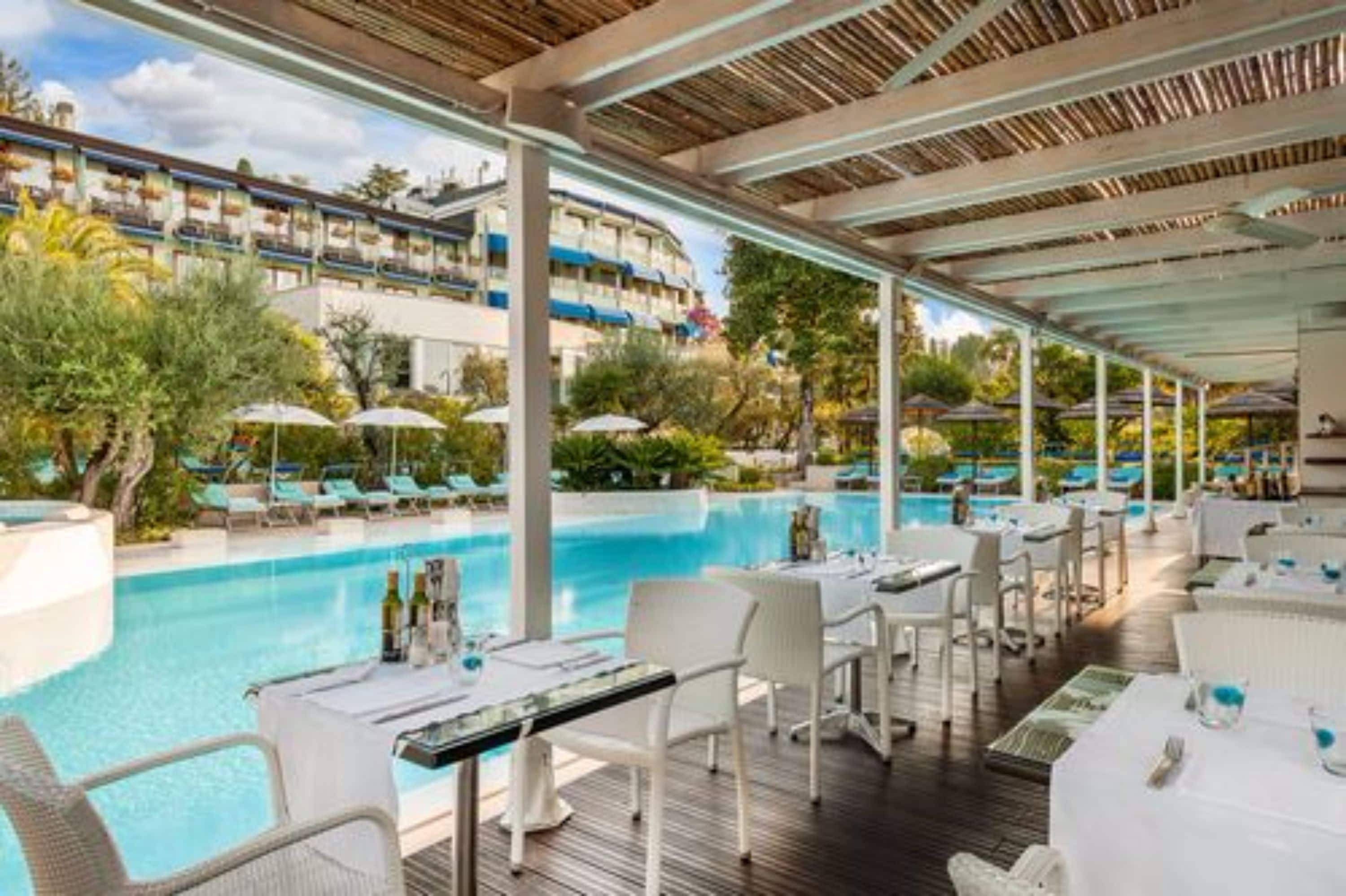 Un restaurant situé au bord de la piscine, avec une terrasse, une piscine et une vue sur un bâtiment d’hôtel.