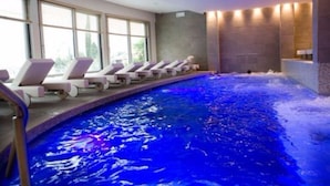 An indoor swimming pool with lounge chairs along the side, large windows, and a stone wall. -  Olivi Hotel & Natural Spa (Sirmione)