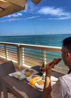 Una mesa de comedor con alimentos para el desayuno y vista al océano.