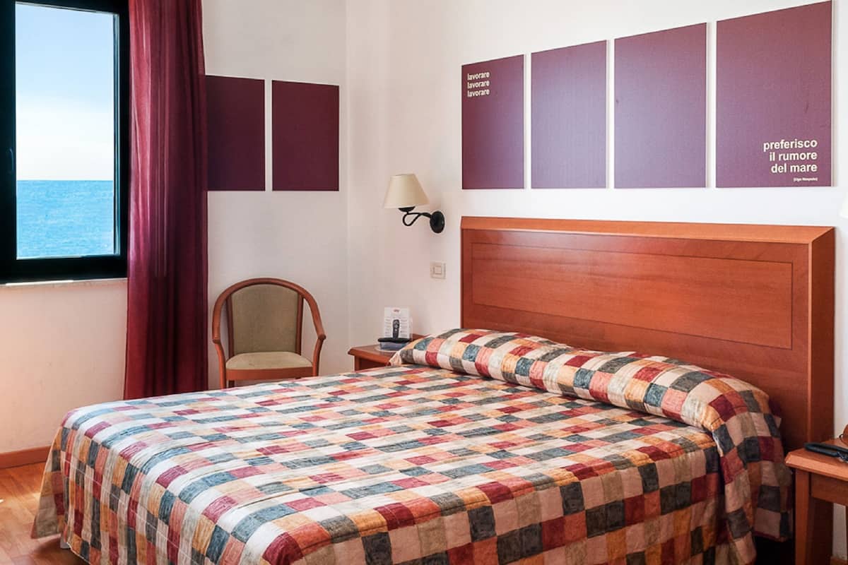 Een hotelkamer met een bed, een stoel, een televisie op een kast en een raam met gordijnen.