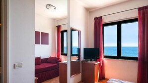 Habitación de hotel con cama, escritorio con televisor, sofá rojo y ventana grande con vista al mar.