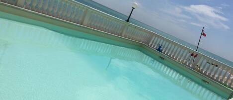 A pool with a clear view of the sea and a white railing.
