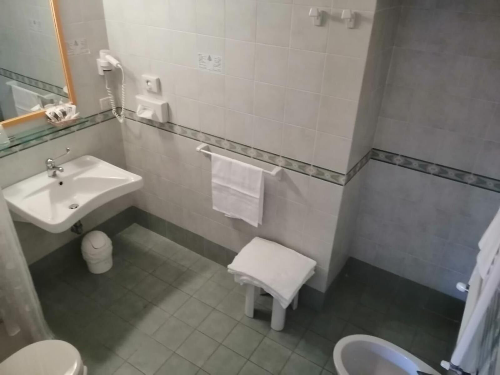 Casa de banho com lavatório, sanita e banheira. Há um porta-toalhas e um pequeno banquinho.