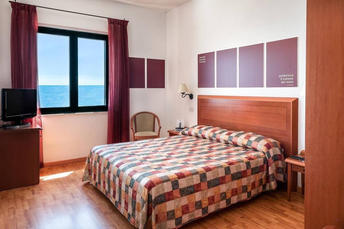 Een hotelkamer met een groot bed, een televisie, een stoel en uitzicht op zee.