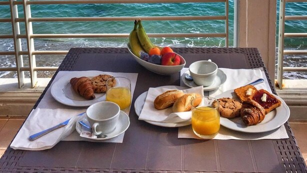 Una mesa con alimentos para el desayuno y vista al océano.