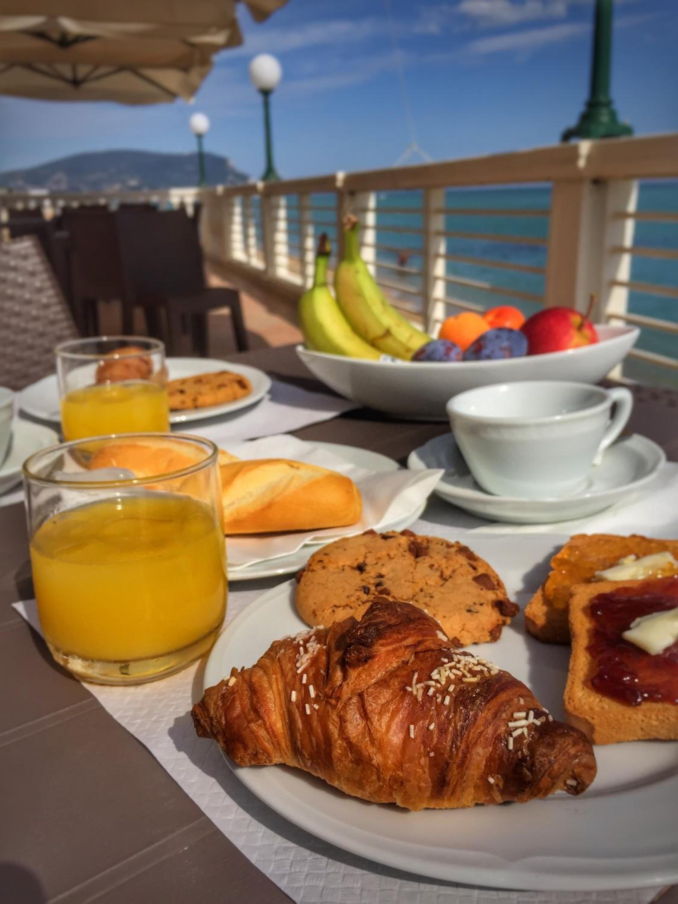 A breakfast table with croissants, cookies, fruit, and orange juice.
