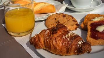 Una mesa de desayuno con croissants, galletas, fruta y jugo de naranja.