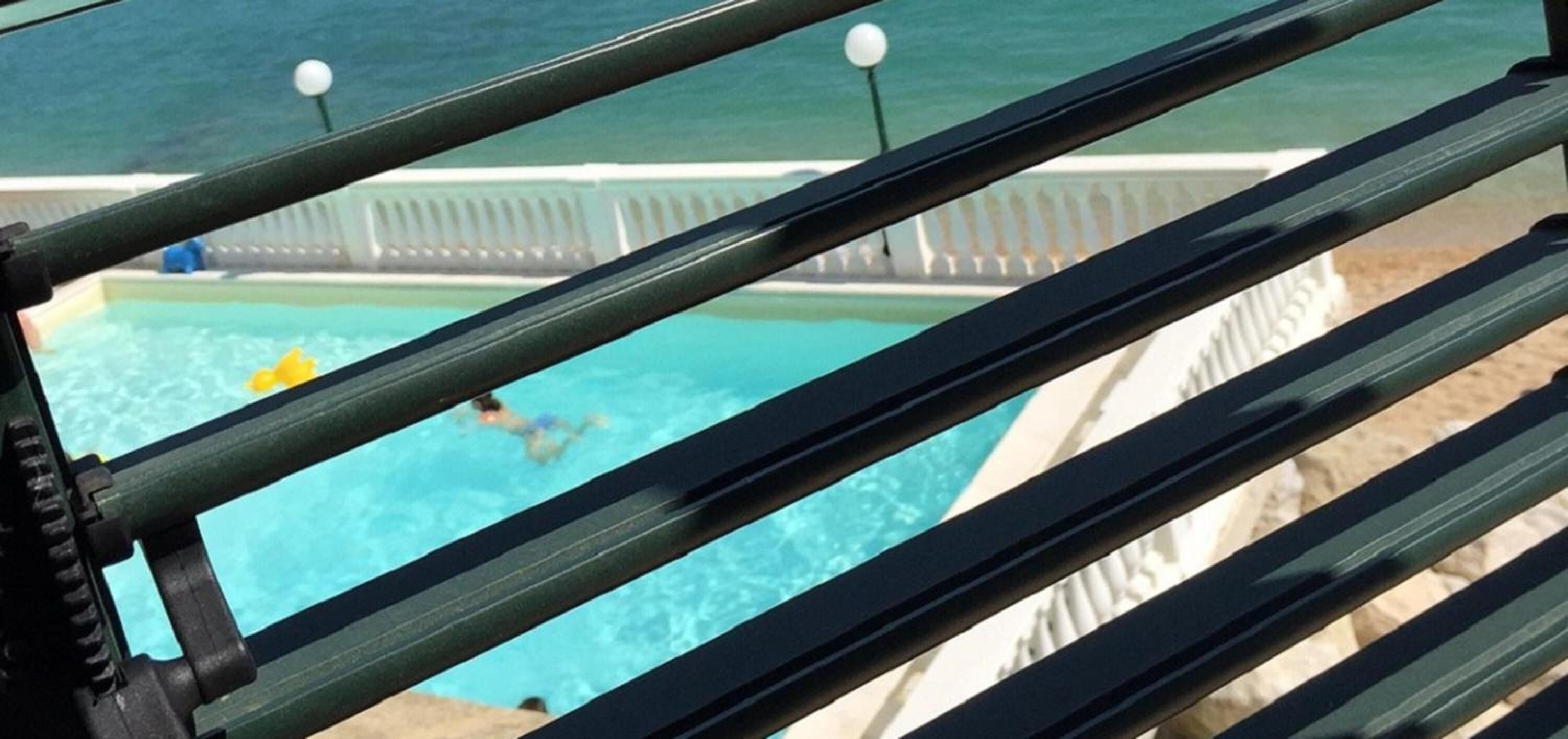 A pool area with clear blue water, a person swimming, and a white fence with a balustrade.
