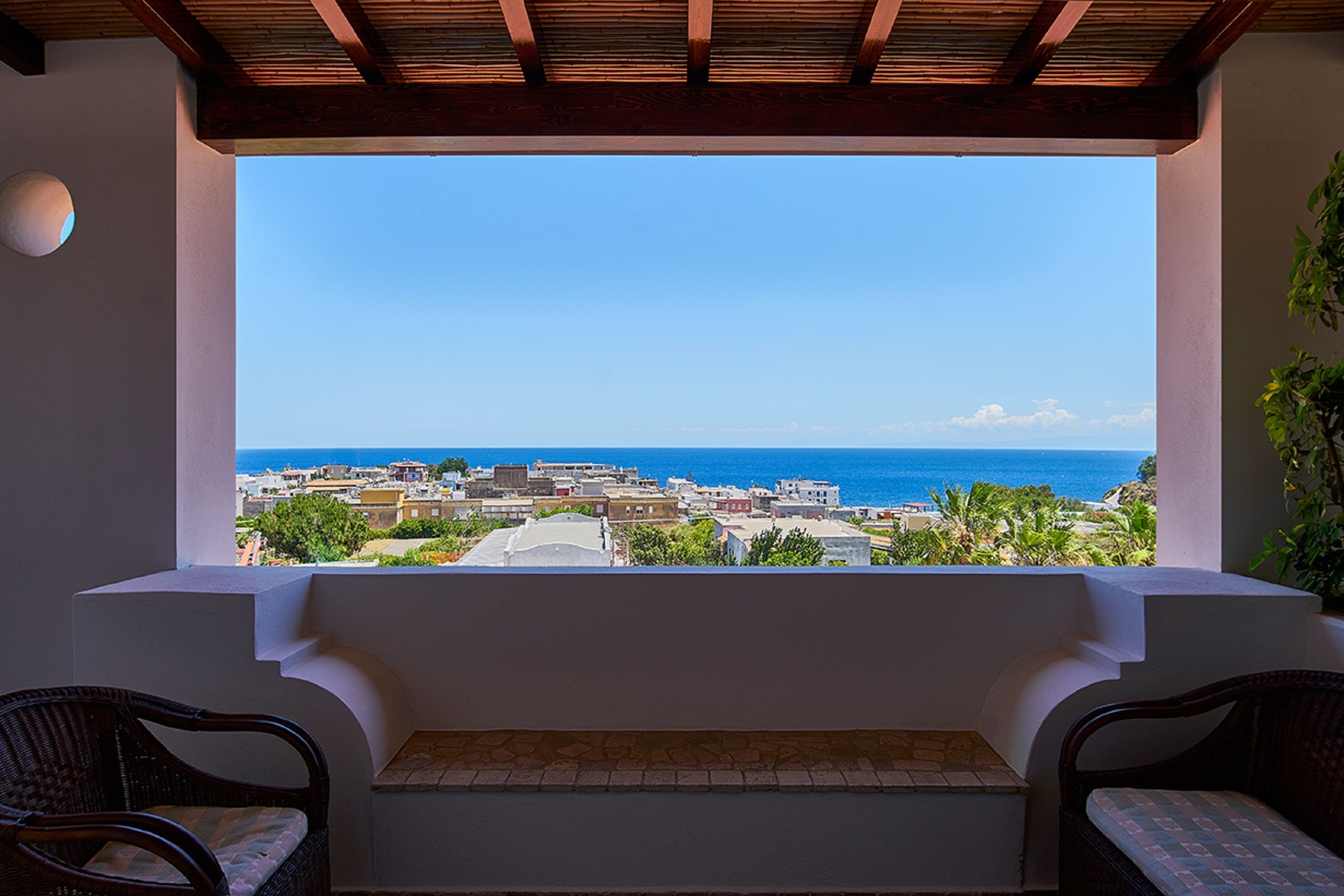Ein Balkon mit zwei Korbstühlen und Blick auf das Meer und die Gebäude.