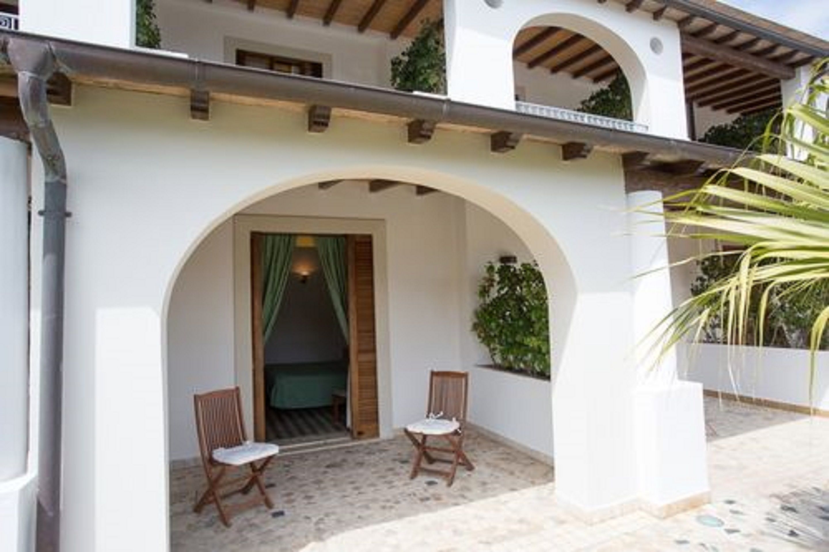 A building with a white facade, an arched entrance, and two wooden chairs outside.
