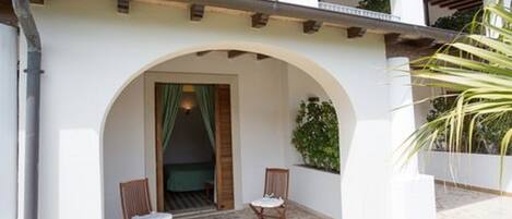 A building with a white facade, an arched entrance, and two wooden chairs outside.