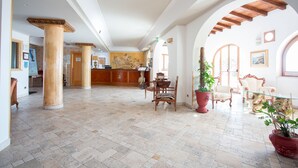 A spacious lobby with a reception desk, classical columns, and a mix of seating areas including a table and chairs. - Hotel Tritone (Lipari)