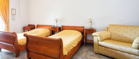 A room with two wooden beds, a sofa, and two bedside tables with lamps.