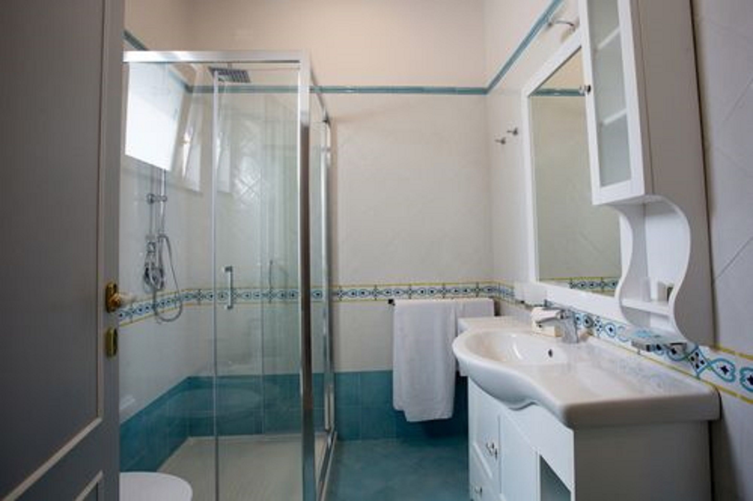 Un baño con cabina de ducha de vidrio, un lavabo blanco y un espejo.