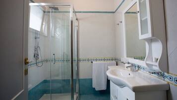 Un baño con cabina de ducha de vidrio, un lavabo blanco y un espejo.