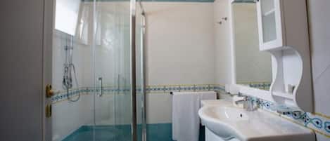 Un baño con cabina de ducha de vidrio, un lavabo blanco y un espejo.
