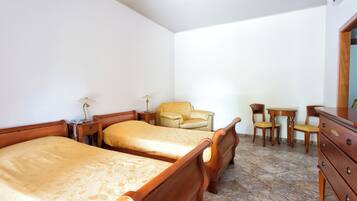Una habitación con dos camas de madera, una silla de madera, una mesita y un aparador.