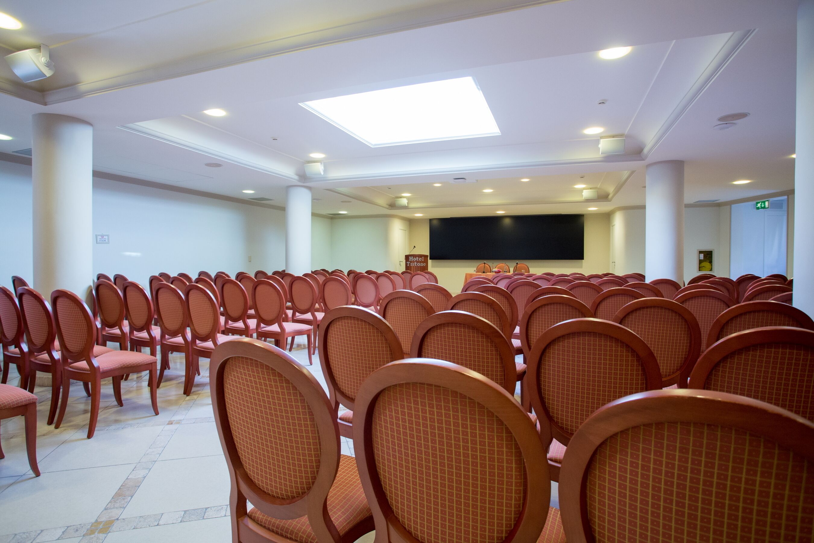 A conference room with rows of chairs, a stage, and a large screen.