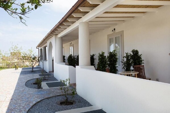 A covered outdoor area with white walls, columns, and potted plants. - Hotel Tritone (Lipari)