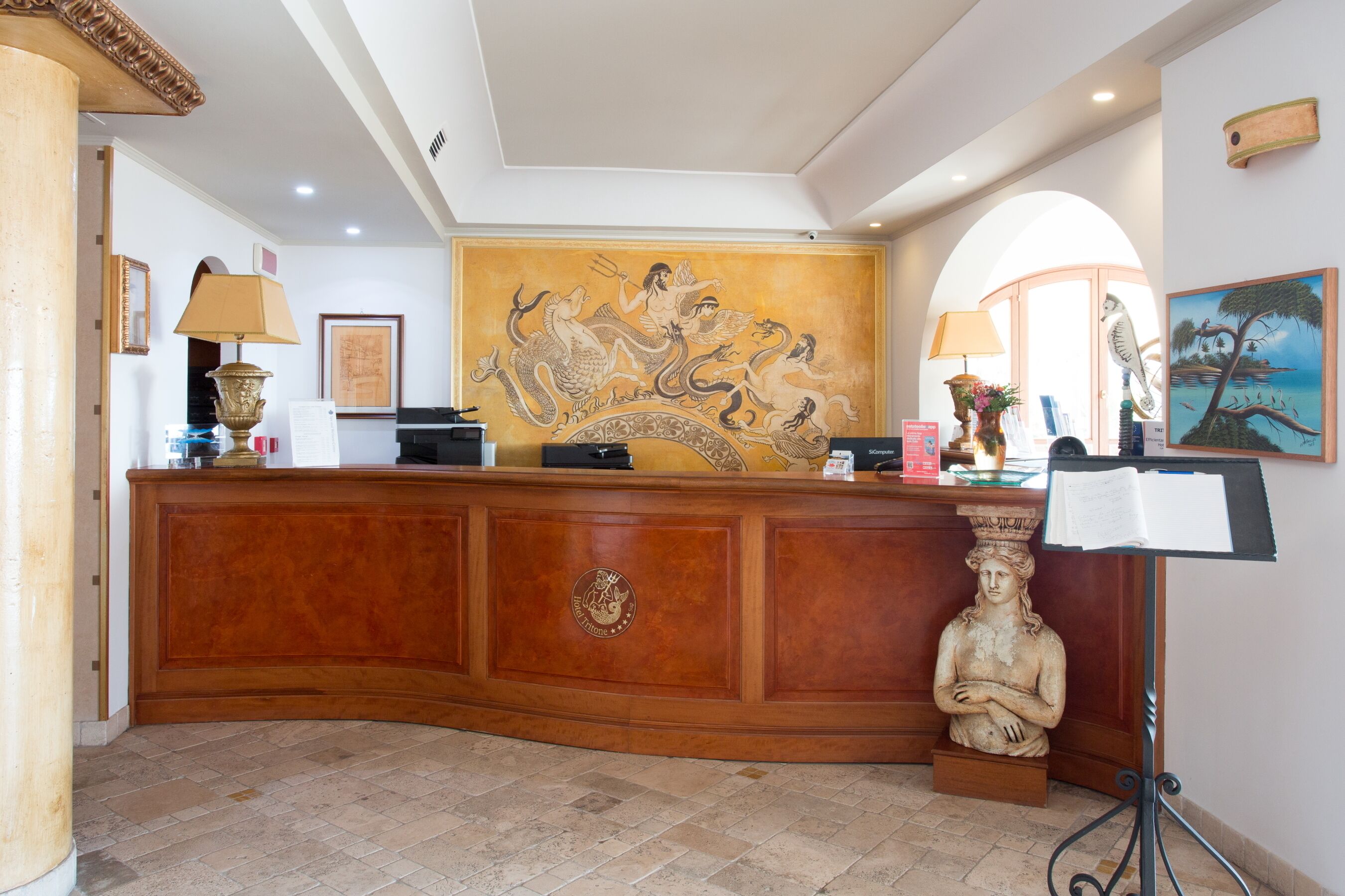 Un área de recepción con un mostrador de madera, un mural grande y una estatua.